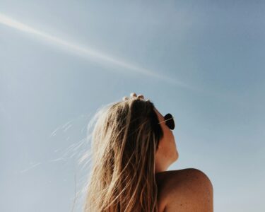 this is the image of a woman wearing sunglasses and looking toward the sun, which is the best source of vitamin D, a vitamin essential for good mental health